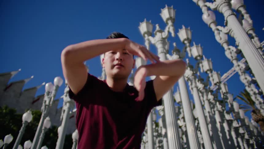 An asian male dancer performs dance moves outside in front of several lamp posts