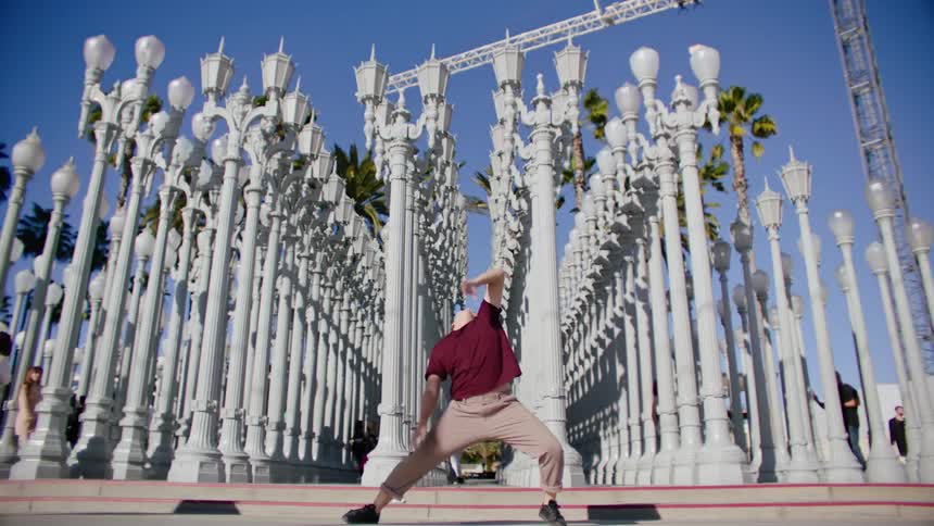 A man dances in front of a row of lamp posts