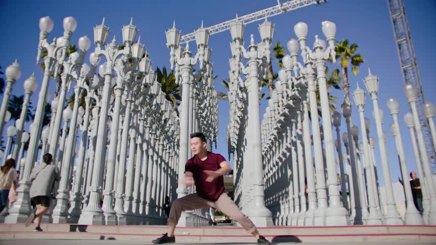 An asian male dancer performs dance moves outside near numerous lamp posts