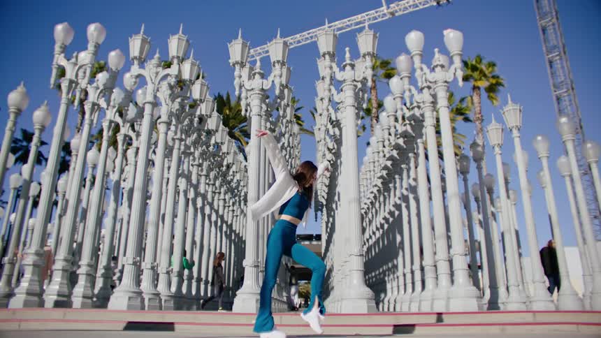 Young woman energetically dancing in front of street lamps on a park in the city