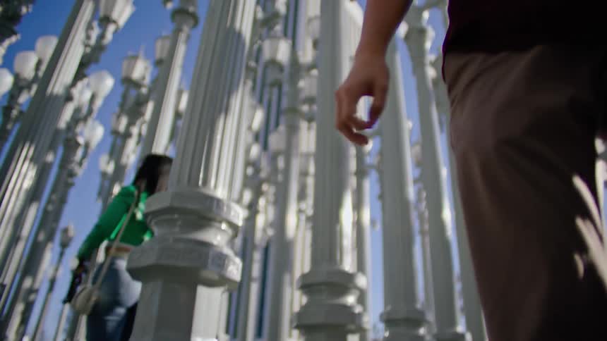 A teenage boy dances outside and a teenage girl turns around and takes a picture of him with her cell phone
