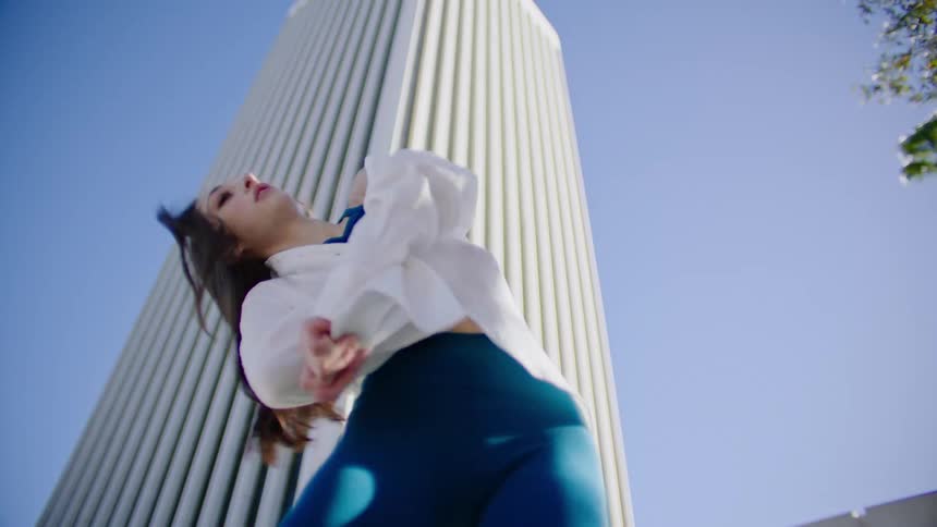 Young woman energetically dancing in front of a white skyscraper in the city