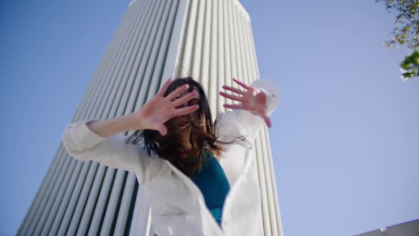 A female dancer performs a series of dance moves outside in front of a tall building