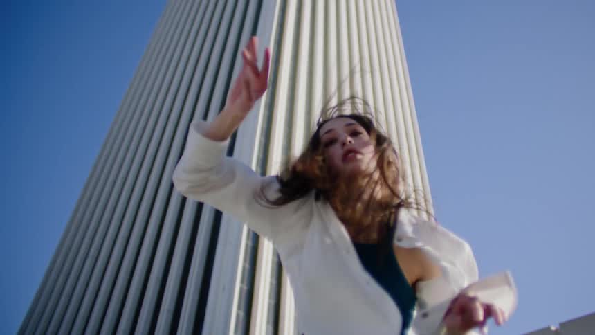Young woman energetically dancing in front of a white skyscraper in the city