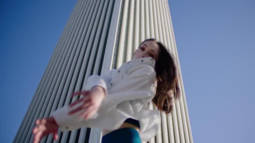 A woman dances hip hop style in front of a skyscraper