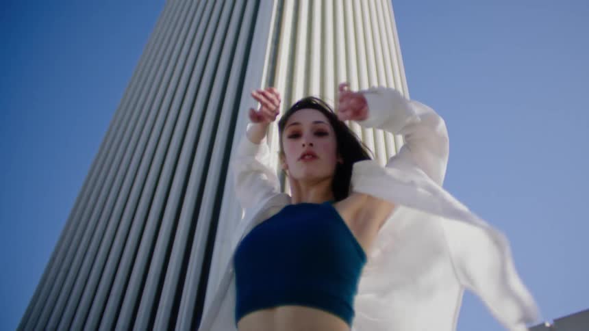 Young woman energetically dancing in front of a white skyscraper in the city