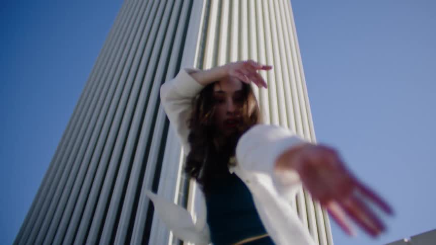 A woman dances in front of a tall skyscraper