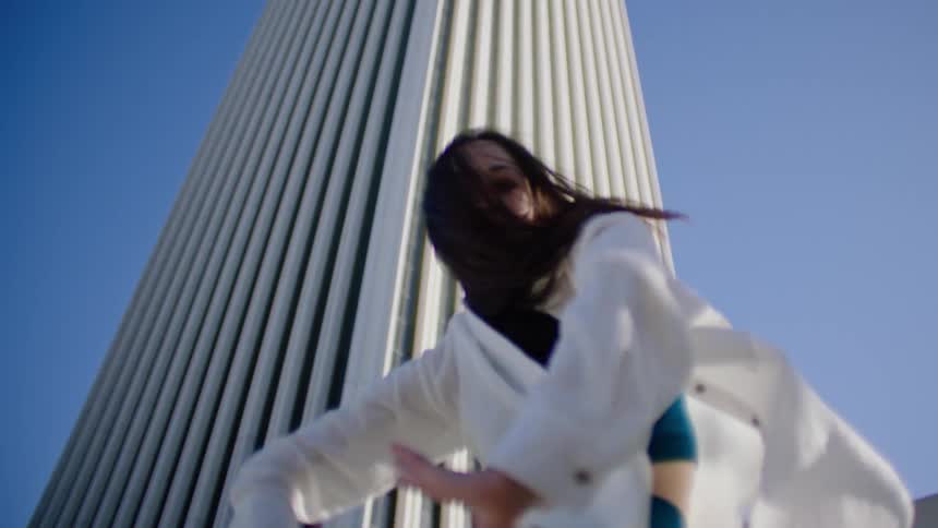 A female dancer performs a series of dance moves outside in front of a tall building