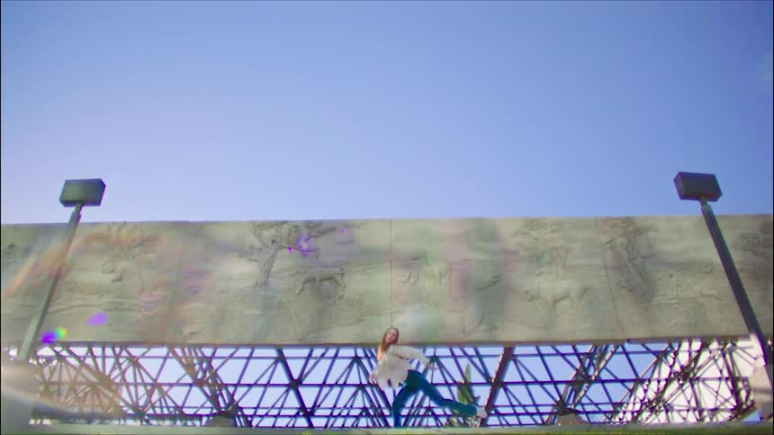 A woman dances in front of a concrete wall
