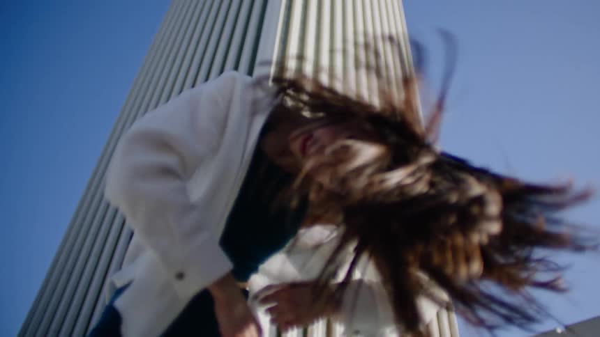 Young woman energetically dancing in reverse in front of a white skyscraper in the city