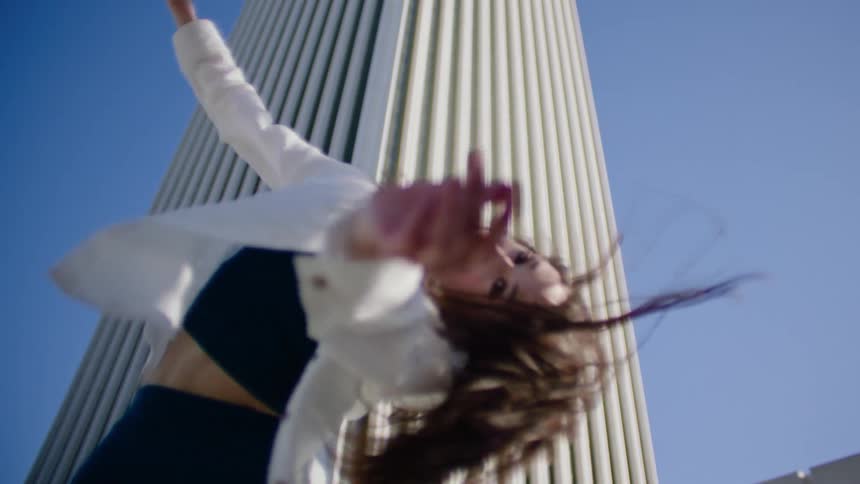 Young woman energetically dancing in reverse in front of a white skyscraper in the city