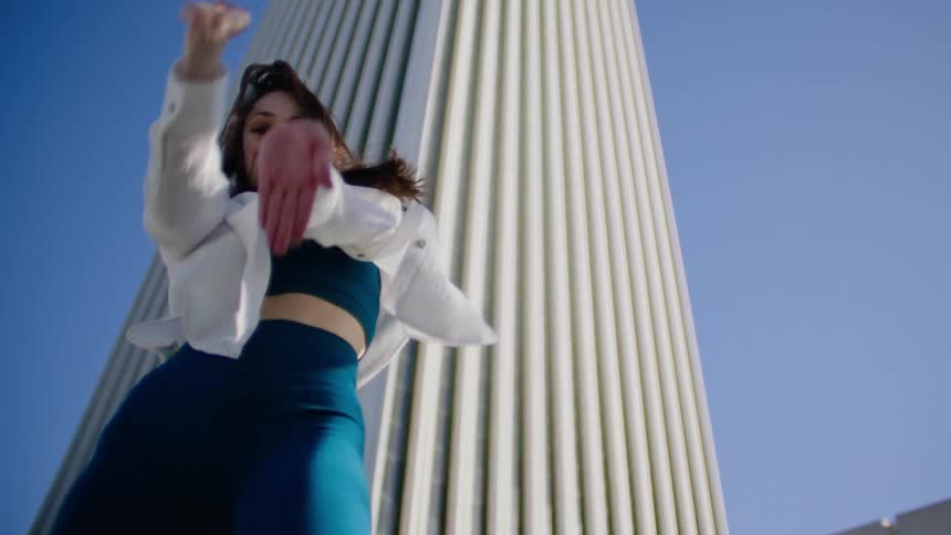 A female dancer performs dance moves while outside in front of a tall building