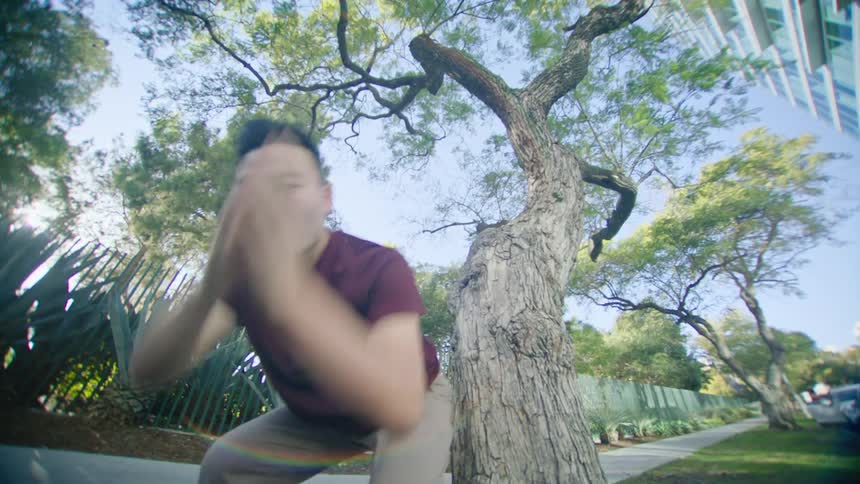 Asian man dancing in front of a tree outdoors in a residential area