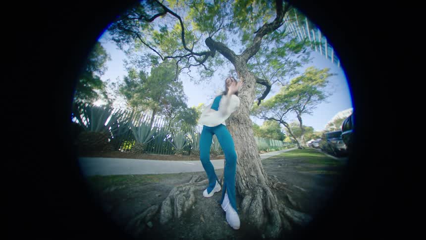 A female dancer performs a series of dance moves outside in front of a tree
