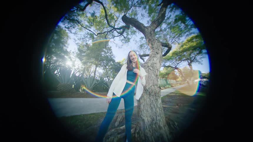 A young woman smiles as she finishes up a dance while she is outdoors under a tree
