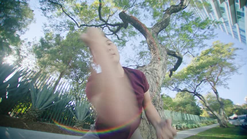 Male dancer with red shirt and brown pants dances next to tree on the sidewalk