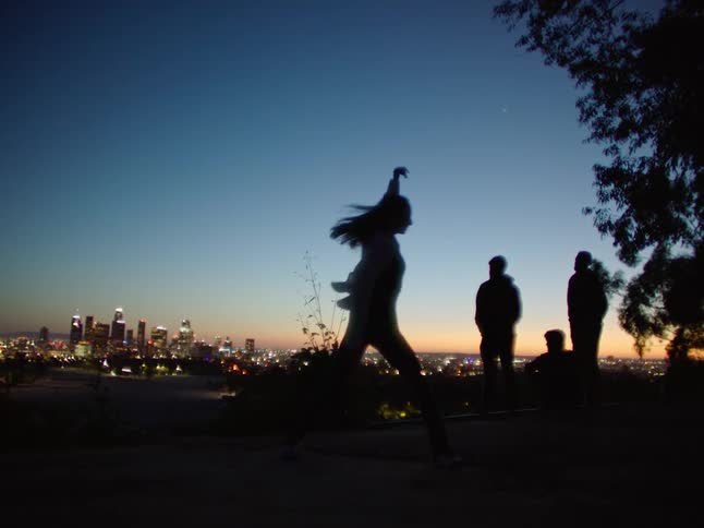 Silhouette of a woman dancing with the view of a big city in the background during sunset