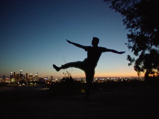 Dancing man is silhouetted against the illuminated skyscrapers and sky at dusk