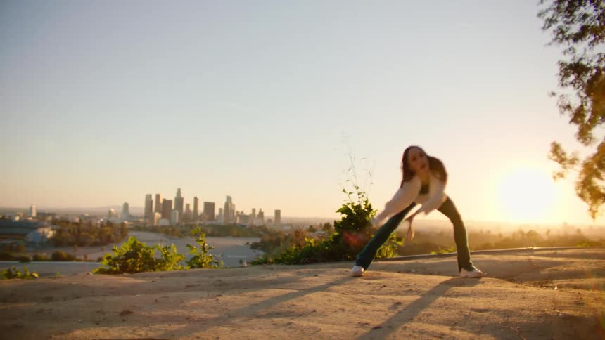 Young woman energetically dancing next to the city skyline at sunset