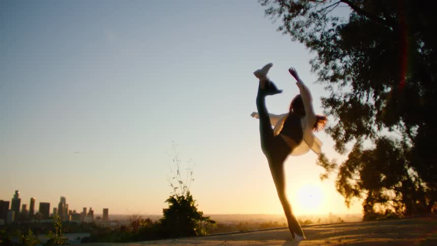 A woman dances in a park with views of downtown