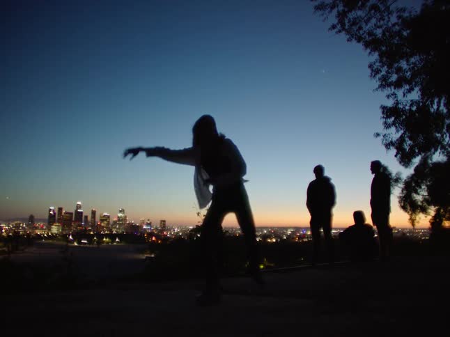 Silhouette of a young woman energetically dancing in front of friends next to the city skyline at sunset