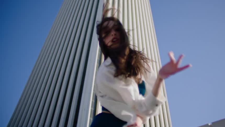 A woman dances and holds a pose with a city skyscraper behind