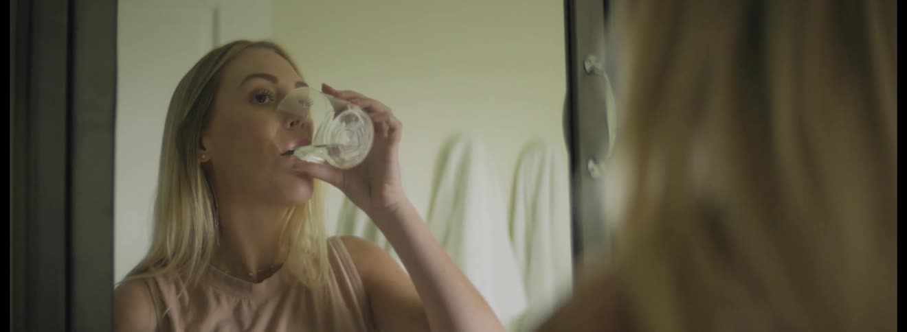 Woman standing in front of a mirror in the bathroom takes a pill with a glass of water