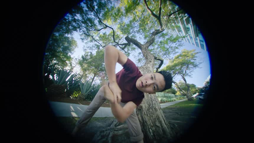 Young asian man energetically dancing in front of a tree in a park at morning through a fish eye lens