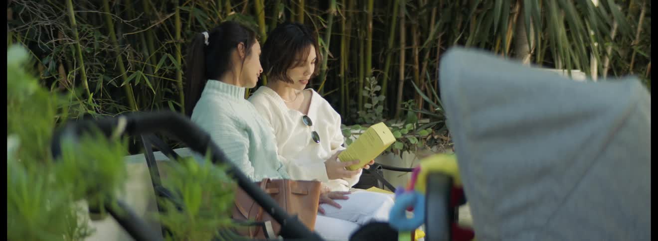 A woman hugs her friend for giving a gift as they sit on a park bench