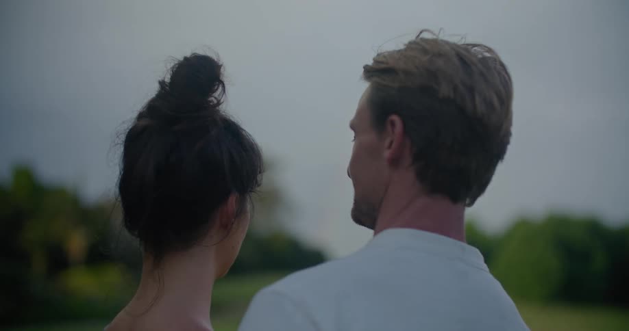 Young couple sitting on the porch looks at the sunset while hugging and kissing