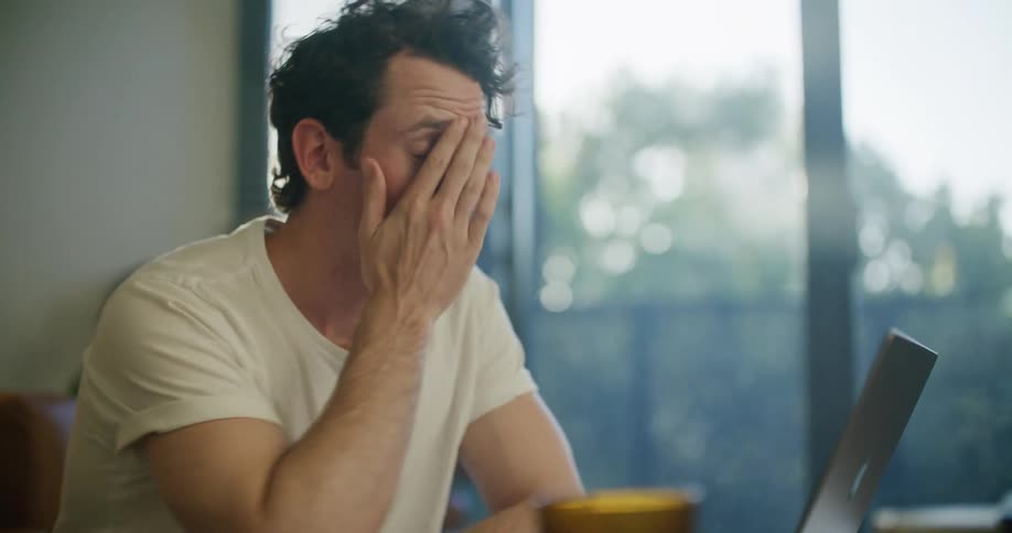 A man rubs his face in frustration while working at home