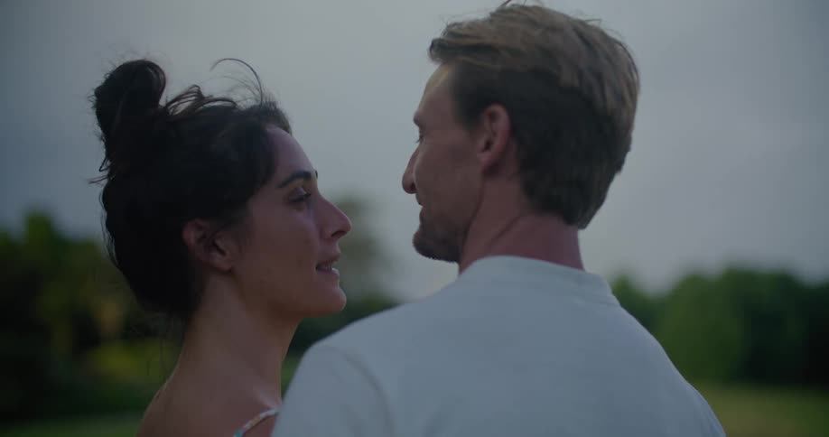 Young couple kisses and hugs while looking at the sunset in the garden