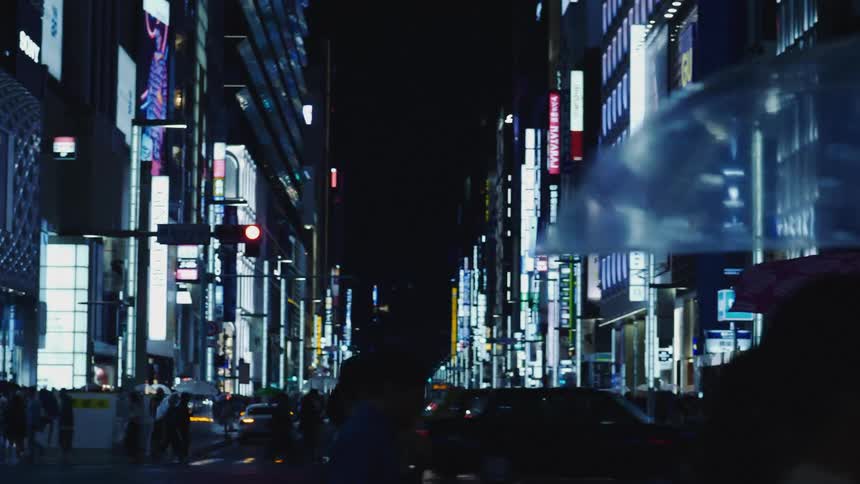 Pedestrians carrying umbrellas walk on the intersection of a big city at night