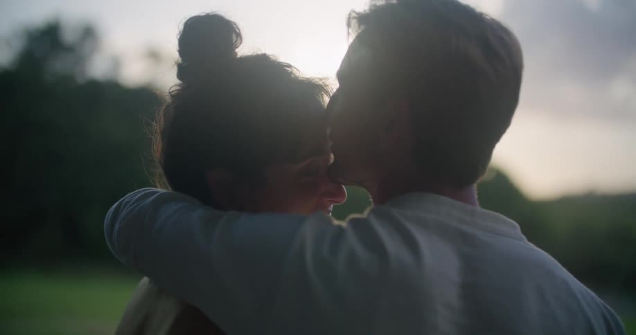 Young couple kissing and hugging while looking at the sunrise in the garden