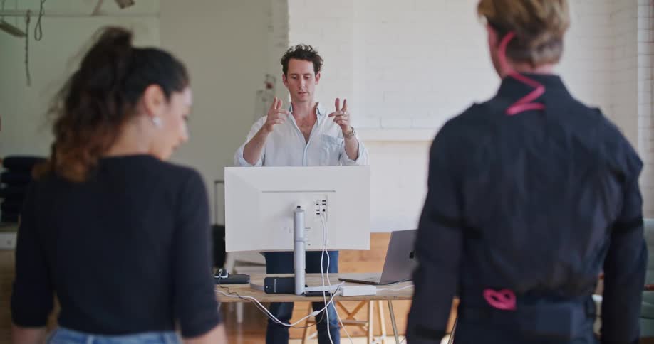 Director in front of a computer gives instructions to a man wearing a motion capture suit