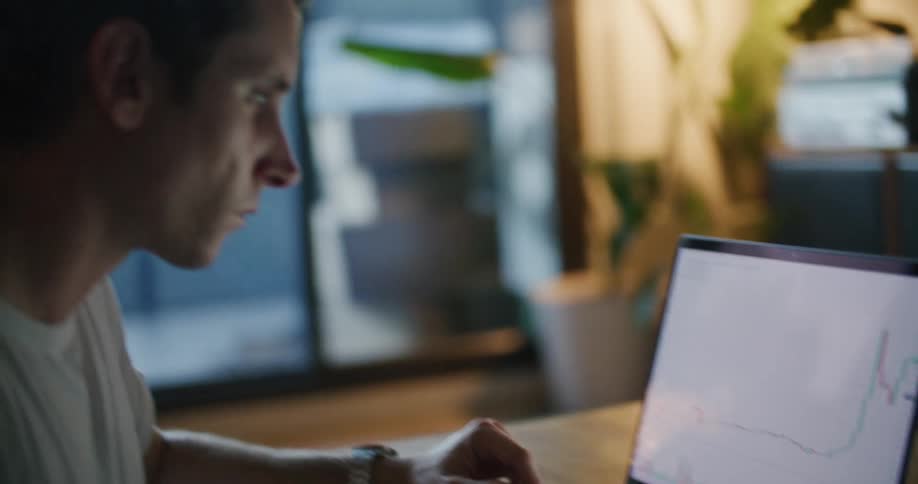 Man consults notebook as he works with computer showing a graph