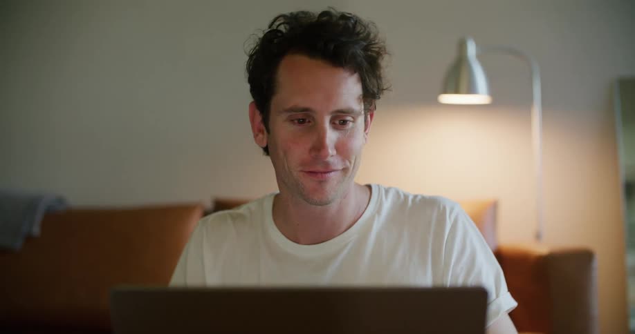 A man types on a laptop while sitting indoors during the day