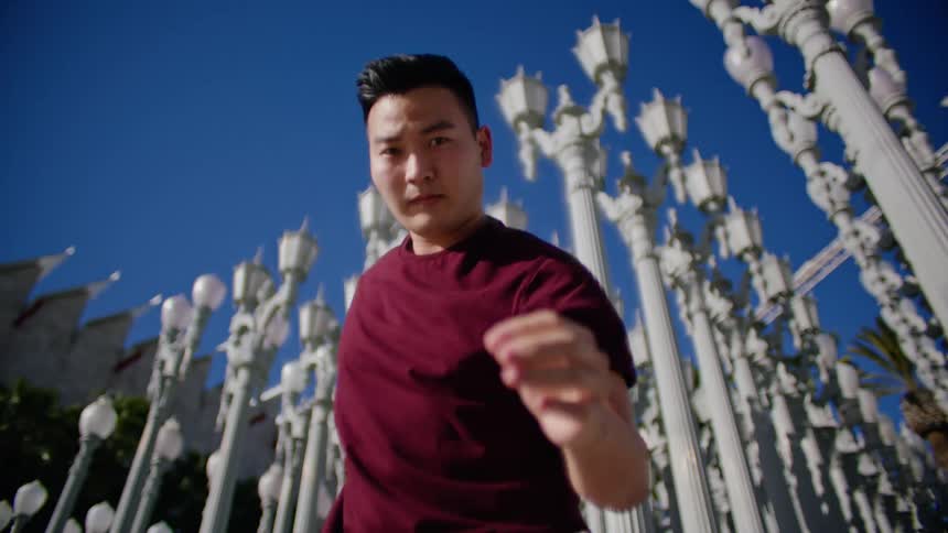 Young asian man energetically dancing in front of a streetlamps on a park under a blue sky
