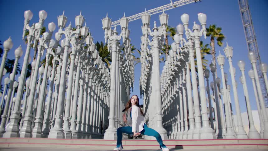 Young woman energetically dancing in front of streetlamps on a park in the city