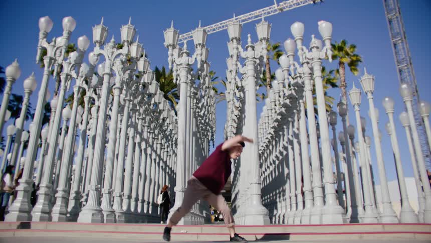 Young asian man energetically dancing in front of a streetlamps on a park under a blue sky