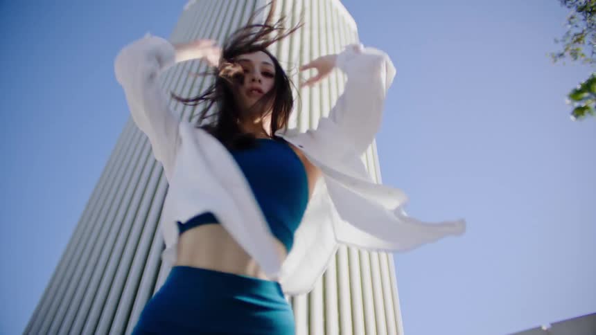 Female dancer with white shirt and teal top and pants dances in front of white skyscraper
