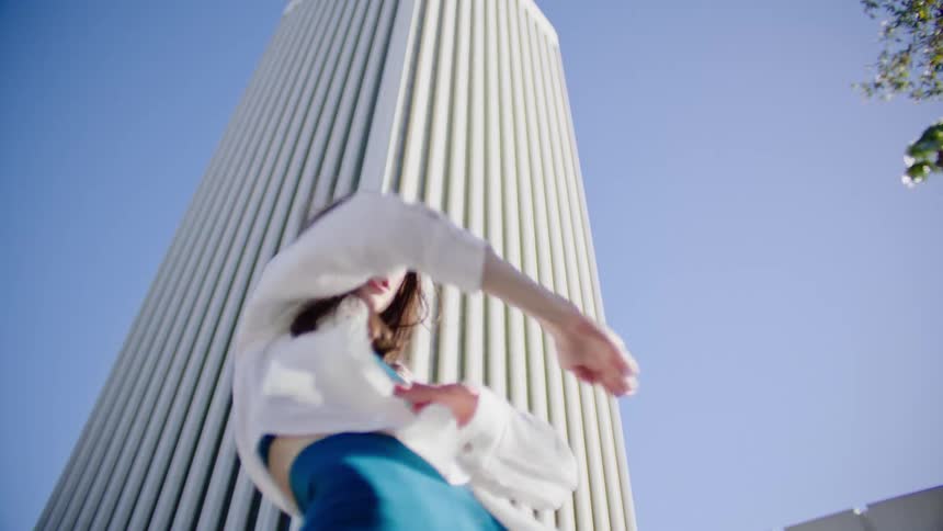 A female dancer performs a series of dance moves outdoors in front of a tall building