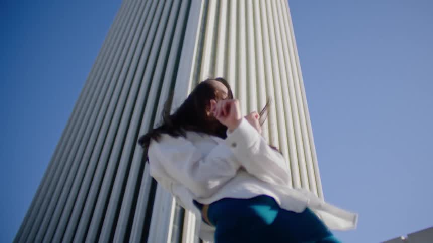 Young woman energetically dancing in front of a white skyscraper in the city