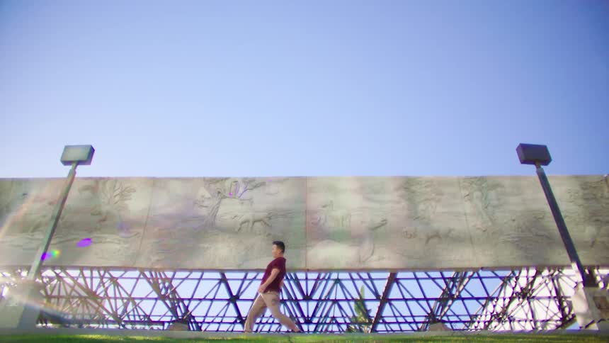 Man in a short sleeved shirt dances outdoors in front of cement murals under a blue sky