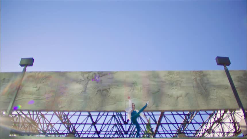 Woman dances in front of stone murals under a blue sky