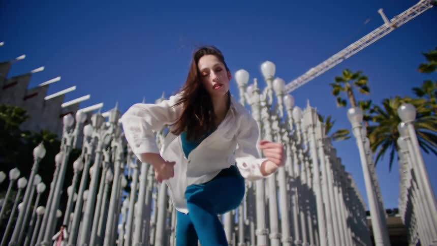 Young woman energetically dancing in front of streetlamps on a park in the city