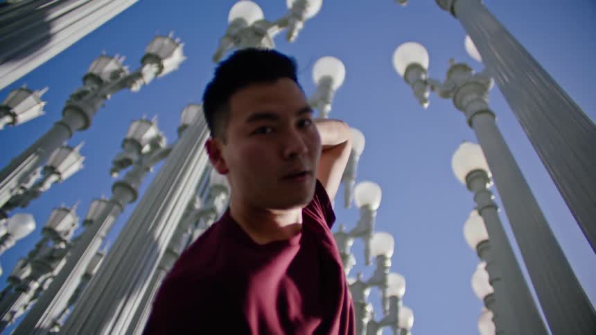 Young asian man energetically dancing in front of a street lamps on a park under a blue sky