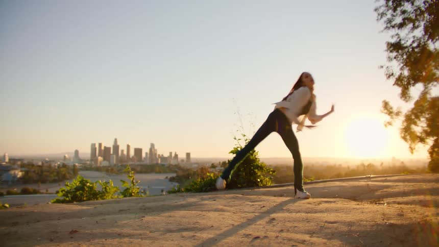 Woman dancing outdoors during sunset with the view of a big city skyline at the background