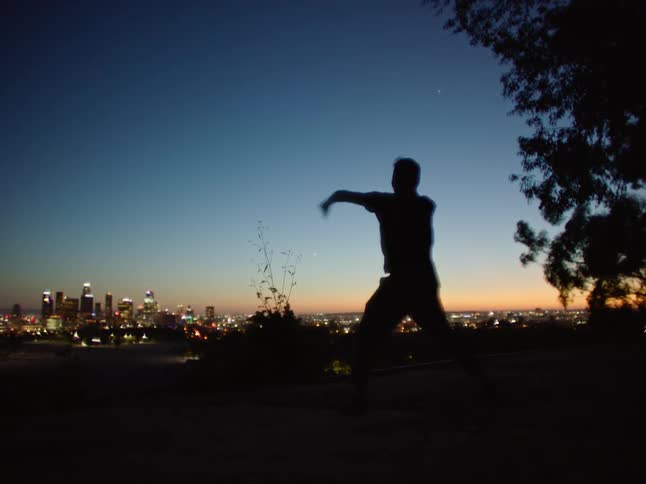 Silhouette of a young man energetically dancing in front of the city skyline at sunset