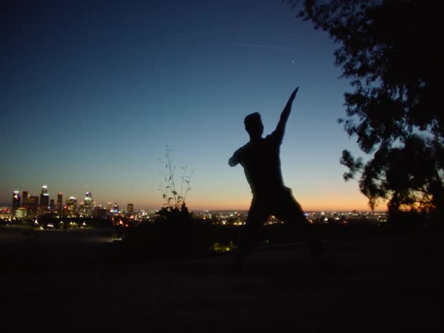 A man dances on a cliff with views of downtown